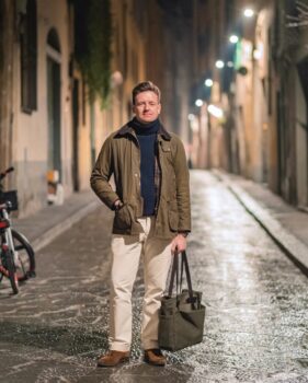 Man in the streets of Florence, Italy, wearing white chinos, suede chukka boots, heavy navy turtleneck and green Barbour jacket